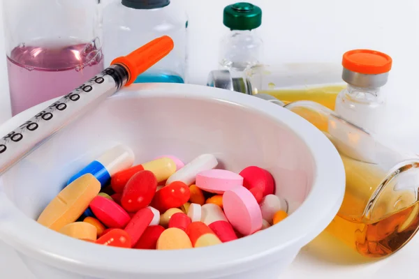 Muitas pílulas coloridas, cápsulas e seringa em um copo com uma colher e frasco de vacina . — Fotografia de Stock