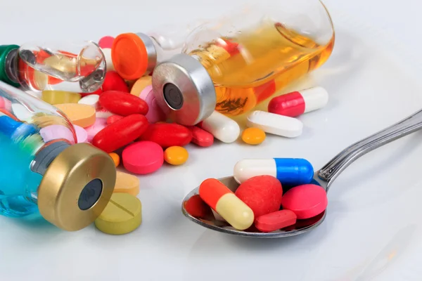 Muitas pílulas coloridas, cápsulas, seringa e frasco em um prato com uma colher . — Fotografia de Stock