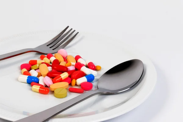 Sok színes tabletták, kapszulák és fecskendő egy edényben egy kanállal és villával. — Stock Fotó