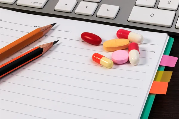 Pillole, capsule, quaderni, matite e tastiera per computer su tavolo di legno . — Foto Stock
