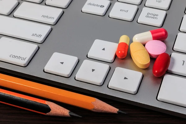 Pillole, capsule, matite e tastiera per computer su tavolo di legno . — Foto Stock