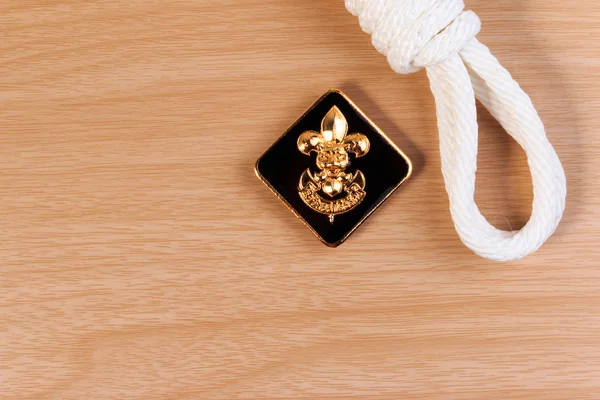 Orderliness white scout rope with vintage boy scouts badge on wooden table. — Stock Photo, Image