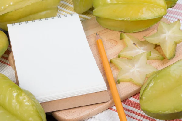 Star apple or averrhoa carambola and notebook on wooden block. Fresh star apple fruit and on wood table. — Stock Photo, Image