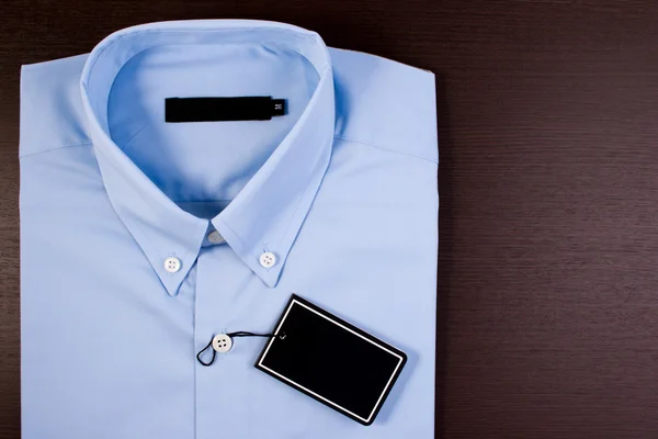 木制背景的蓝色衬衫。蓝色衬衫，黑色空白价格标签. — 图库照片