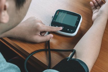 Evde kan basıncı, nabız ve kalp atışlarını ölçmek için dijital sfenometre kullanan bir adam var. Erkek sağlığı, kan basıncını dijital basınçla ölçer ve tansiyonu ölçer. Hipotansiyon kavramı.