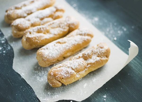 Cakes eclairs with powdered sugar on parchment paper — Stock Photo, Image