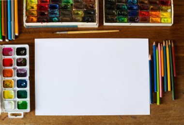 Artist`s table with blank sheet of paper and art tools, flat lay, selective focus, artist`s tools, art supplies, pencils, paintbrush, watercolor paints