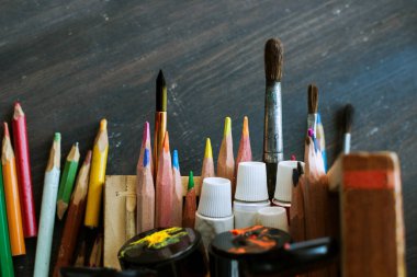 Artist`s tools, art supplies, pencils, paintbrushes, paints on wooden background, selective focus