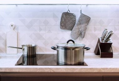 Modern simple home kitchen with induction hob, stainless kitchen utensils and soft lighting, selective focus