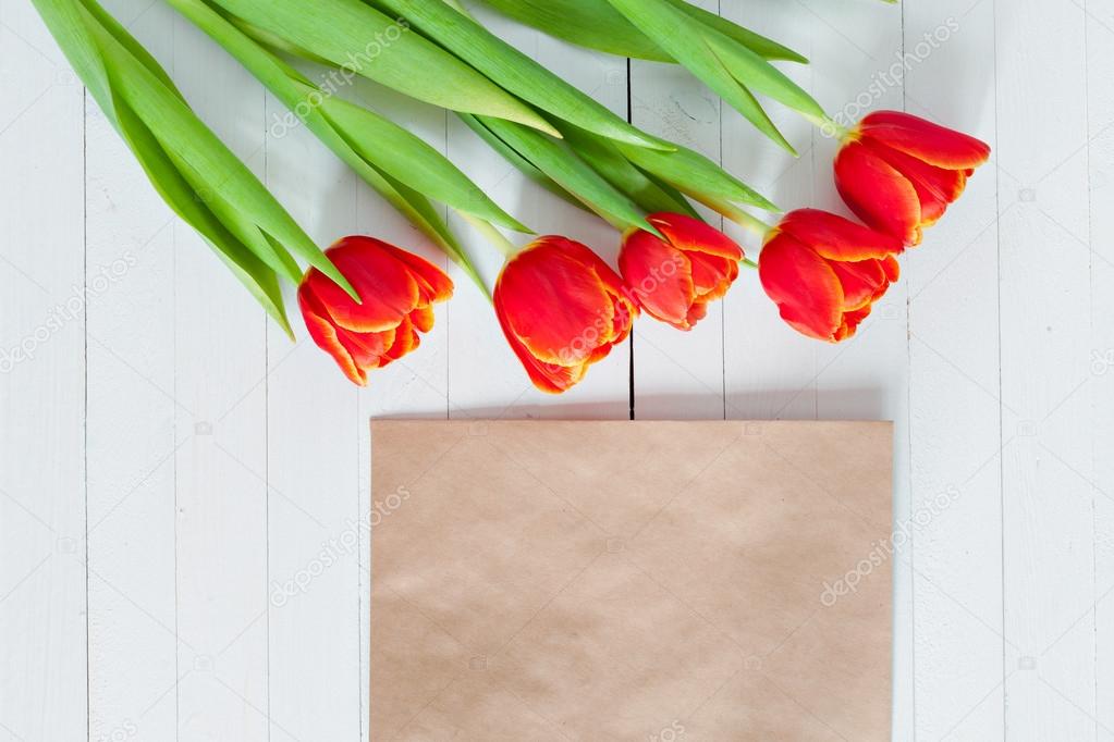 Colorful tulip bouquet and blank greeting card. Top view over white wooden table