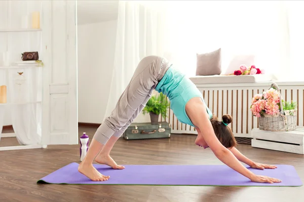 Yoga exercises. Young caucasian woman staying in a pose on the mat downward dog — Stockfoto