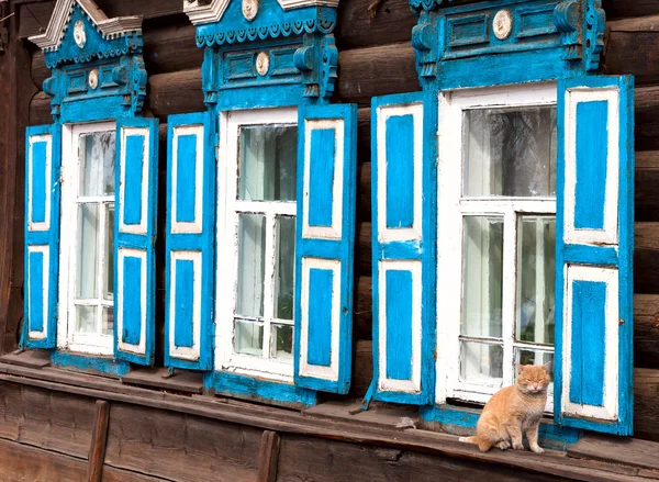 Vieille maison russe en bois façade en rondins naturels, volets bleus en bois sur les fenêtres. Graine de chat rouge sous la fenêtre . — Photo