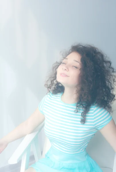 Portrait of a happy young girl with curly hair in a white chair. Morning room and light. Misty picture. Enjoy life — Φωτογραφία Αρχείου