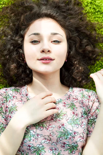 Portrait d'une jeune belle fille aux cheveux bouclés couché sur le sol sur un tapis pour s'asseoir dans la salle de soleil lumineuse. Grands yeux verts et cheveux bruns ondulés . — Photo