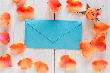 Beyaz ahşap arka plan üzerinde bir imza için alan ile romantik inci mavi zarf. Kopyalama alanı ile. Aşkın tanınmasına mektup. Zarfın etrafında pembe gül yaprakları.