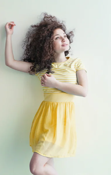 Mladé děvče z kavkazského vzezření tančí a sní o světlé místnosti v letním dni. Vlnité vlnité vlasy a žluté šaty. Odpočívej a buď šťastný. — Stock fotografie