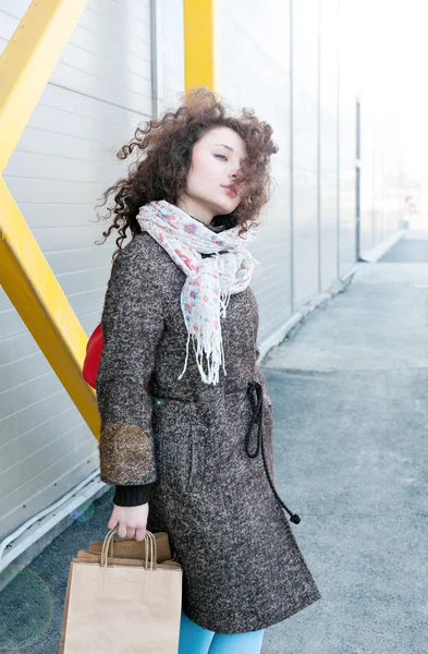 Happy girl finishes shopping. In the hands packages with purchases. Girl in a coat in the spring, wavy curly hair is developing the wind, full portrait outdoors growth. Make purchases with pleasure. — Stock fotografie