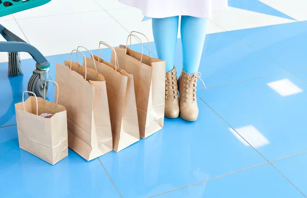 ショッピングバッグの近くに水色のタイツとベージュの靴を履いている女性の足。ショッピングモールでの買い物。いたずらな気分。スペースをコピーします。脚とバッグ — ストック写真