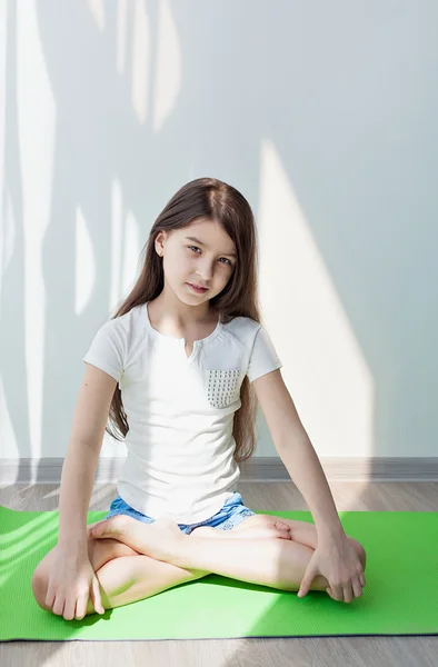 小女孩在绿色的瑜伽垫上做体操。做健身运动，在白色背景。儿童健身，儿童瑜伽 — 图库照片