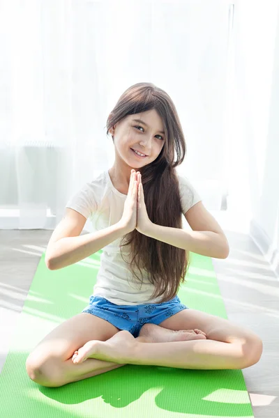 Little girl doing gymnastics on a green mat for yoga. childrens fitness, yoga for children. doing fitness exercise and stretching in a bright room. lotus Pose — Stock Photo, Image