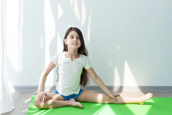 Маленькая девочка, занимающаяся гимнастикой на зеленом коврике для йоги, занимающаяся фитнесом и растяжкой. фитнес и йога для детей . — стоковое фото