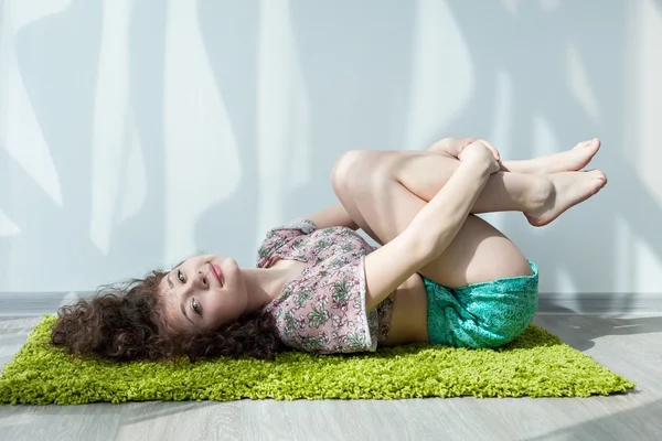 Yeşil halıda yerde kıvırcık saçlı genç kız, esneme egzersizleri yapıyor. Parlak güneş odasında sabahları egzersiz yapıyor. Meditasyon. Evde yoga pratiği yap. Hayatın tadını çıkar..