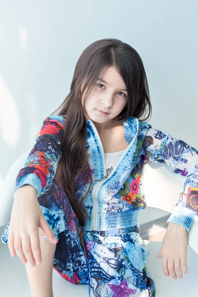 Portrait of a little girl of fashion baby on a white chair. Stylish little girl with long hair sitting on a white chair in front of the camera. Photo model child cool fashionable. Carefree fun — Stock Photo, Image