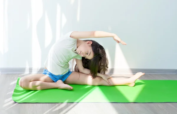 küçük kız bir yeşil yoga mat jimnastik yapıyor. Fitness egzersizleri ve germe. Çocuk fitness ve yoga çocuklar.