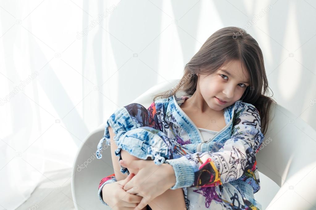 Portrait of a little fashion kid girl on a white chair. Stylish 