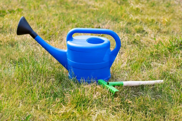 Kolorowy ogród narzędzia, niebieskie plastikowe konewka i rake. — Zdjęcie stockowe
