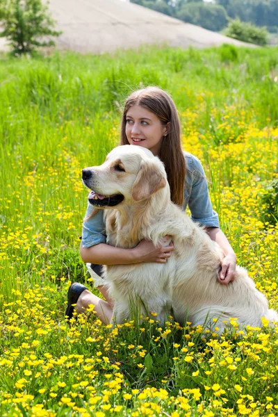 Nő és a golden retriever, sárga virágok területén. — Stock Fotó