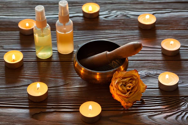 Ciotola per cantare su sfondo di legno scuro. Candele accese e olio per aromaterapia e massaggio .. — Foto Stock