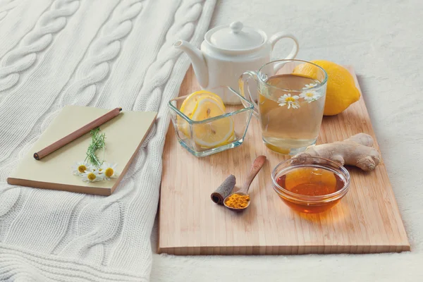 Bylinkový čaj v sklenici s květy heřmánku, kurkuma a medu na dřevěném prkénku. Léčba se studeným nápojem. Léčba lidových prostředků v posteli. Kniha čtení — Stock fotografie