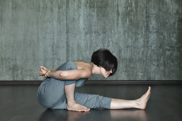 Junge Frau praktiziert Yoga auf einem Hintergrund aus grauer Betonwand. Urbaner Hintergrund. Monochromes Bild. — Stockfoto