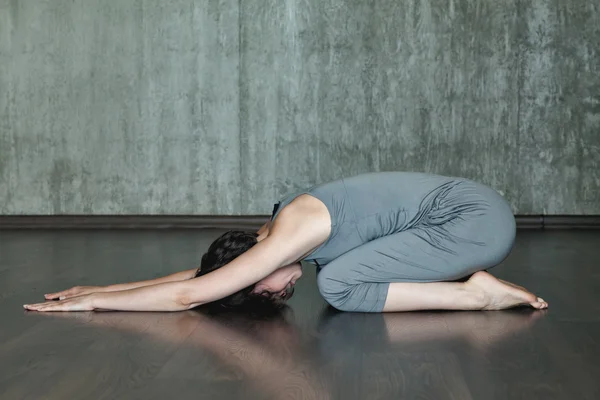 Junge Frau praktiziert Yoga auf einem Hintergrund aus grauer Betonwand. Urbaner Hintergrund. Monochromes Bild. — Stockfoto