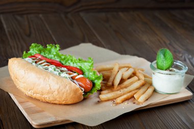 Ahşap arka plan üzerinde parşömen üzerinde sos ve Patates kızartması ile sosis ve sebze ile büyük lezzetli sosisli. gurme için sosisli sandviç.