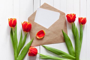 Kırmızı lale buket bahar ve bir kart kopya alanı ile beyaz ahşap zemin üzerinde bir zarf içinde. İmza yeri olan üstten görüntülemek.