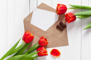 Kırmızı lale buket bahar ve bir kart kopya alanı ile beyaz ahşap zemin üzerinde bir zarf içinde. İmza yeri olan üstten görüntülemek.