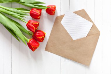 Kırmızı lale buket bahar ve bir kart kopya alanı ile beyaz ahşap zemin üzerinde bir zarf içinde. İmza yeri olan üstten görüntülemek.