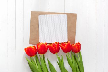 Kırmızı lale buket bahar ve bir kart kopya alanı ile beyaz ahşap zemin üzerinde bir zarf içinde. İmza yeri olan üstten görüntülemek.