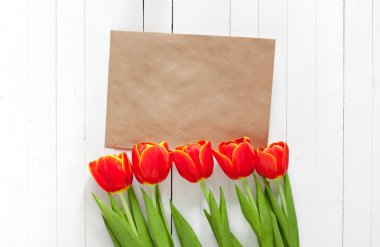 Kırmızı lale buket bahar ve bir kart kopya alanı ile beyaz ahşap zemin üzerinde bir zarf içinde. İmza yeri olan üstten görüntülemek.