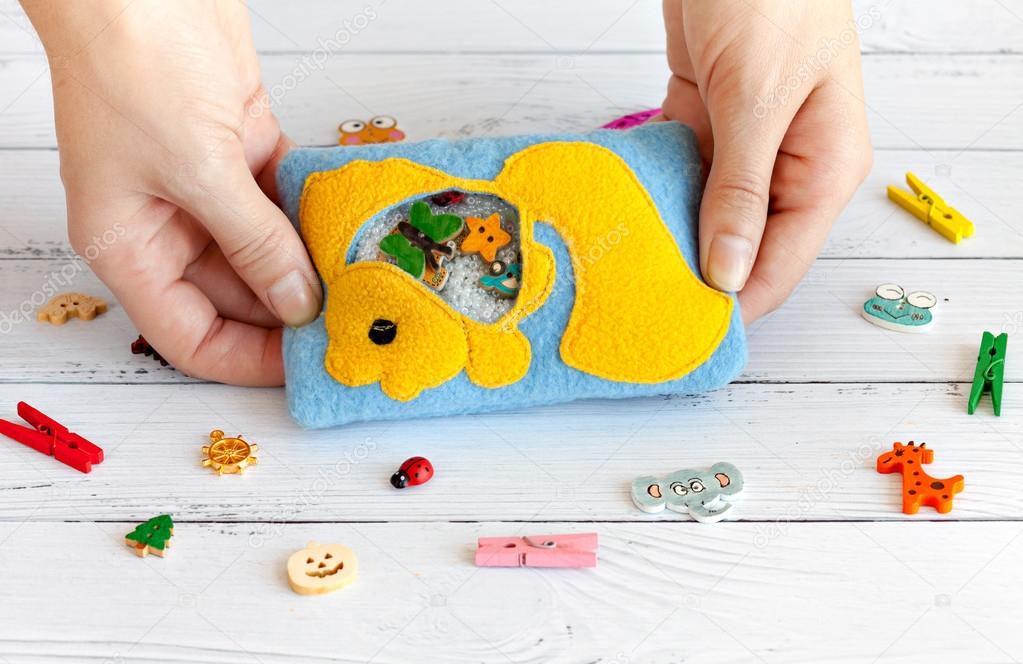 Childrens toy made of colored fleece for the development motor skills in the hands women. Bag with yellow fish filled plastic beads and figurines on a white wooden background. handmade toys