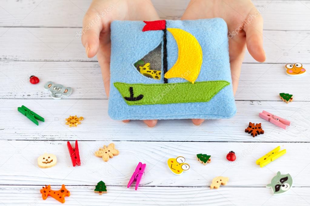 Childrens toy made of colored fleece for the development motor skills in the hands women. Pouch with a ship the filled plastic beads and figurines on white wooden background. handmade toys.