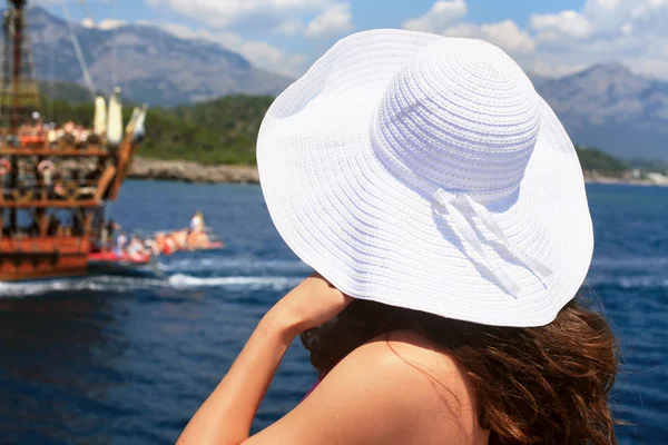 Femme dans un grand chapeau blanc debout près de la rampe et regarde — Photo