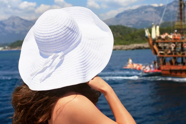 Femme dans un grand chapeau blanc regarde un navire en mer — Photo