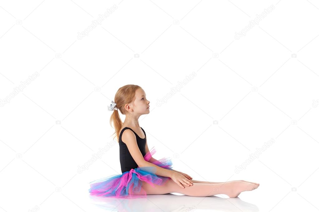 ittle ballerina sitting on floor on white backgroundn studio pos