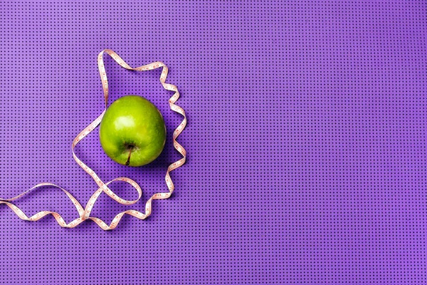 Green apple and measuring tape. Purple yoga mat.