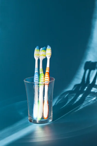 Três escovas de dentes coloridas em um copo — Fotografia de Stock