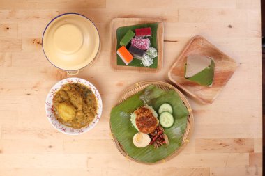 Nasi Lemak kokulu hindistan cevizi sütü sambal arkadaşı fıstık ançüezli yumurta sarılı muz yaprağı bambu tabağı renkli nyonya kuih tatlı çöl palmiyesi yaprağı ahşap arka planda