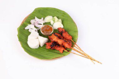 Tavuklu sığır eti, Satay ile tanış Nasi empitli pirinç keki dilimlenmiş soğan salatalığı tatlı fıstık sosu muz yapraklı bambu sepeti beyaz arka planda.
